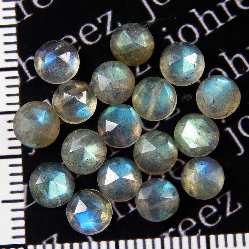May include: A collection of 18 faceted labradorite gemstones, each with a unique iridescent sheen. The stones are a mix of light and dark gray with flashes of blue and green.