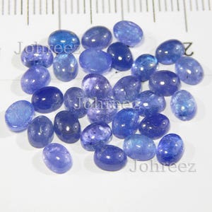 Op de afbeelding: Een verzameling van 25 ovale, blauwe edelsteen cabochons. De stenen zijn glad en gepolijst, met een lichte variatie in kleur en grootte.