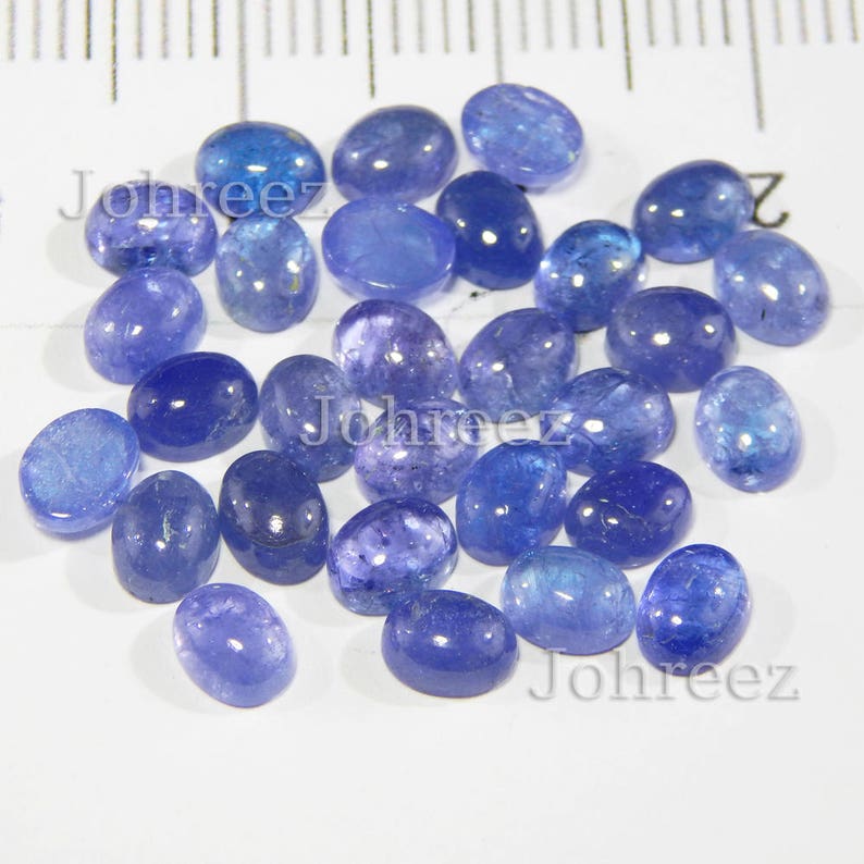 Op de afbeelding: Een verzameling van 25 ovale, blauwe edelsteen cabochons. De stenen zijn glad en gepolijst, met een lichte variatie in kleur en grootte.