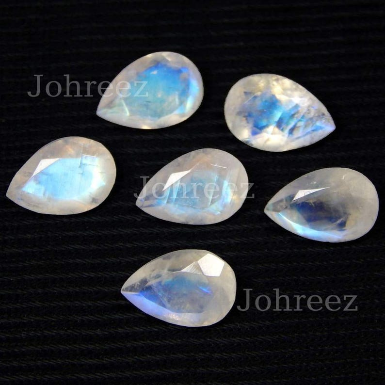 May include: Six pear-shaped moonstone gemstones with iridescent blue and white colors. The stones are faceted and have a smooth, polished finish.