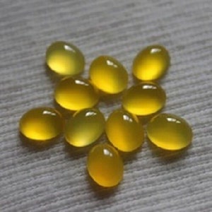 May include: A collection of nine smooth, oval-shaped yellow gemstones. Each stone features a polished, translucent surface that catches the light, displaying a vibrant, uniform golden-yellow hue across their rounded, cabochon-style forms.