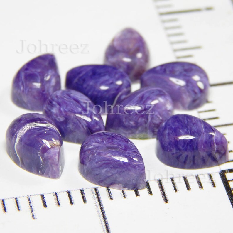 May include: A collection of eight purple and white pearlescent gemstone cabochons. The cabochons are smooth and have a swirling pattern.