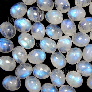 May include: A collection of oval-shaped moonstone cabochons, each displaying a unique iridescent blue sheen. The stones are arranged on a black background.