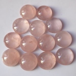 May include: A collection of 12 round, pale pink rose quartz cabochons. The cabochons are smooth and polished, with a slightly translucent appearance.