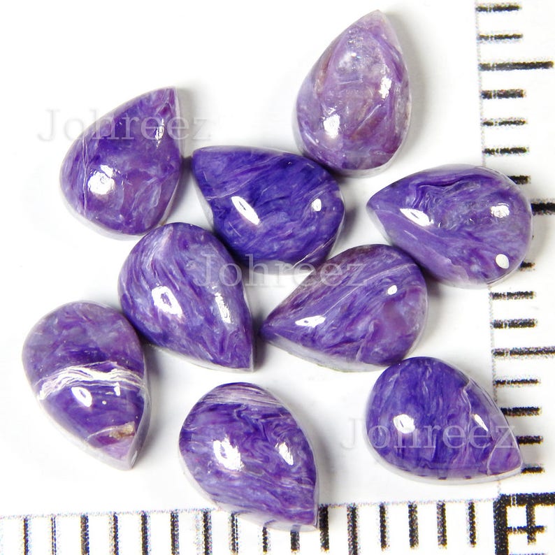 May include: Ten purple and white teardrop-shaped cabochons, likely made of sugilite, a gemstone known for its vibrant purple color and swirling patterns.