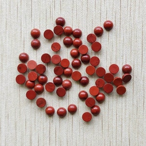 May include: A collection of 30 round, red gemstone cabochons. The cabochons are smooth and polished, with a slight variation in color and pattern.