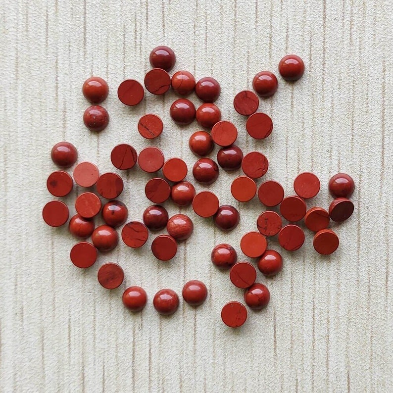 May include: A collection of 30 round, red gemstone cabochons. The cabochons are smooth and polished, with a slight variation in color and pattern.