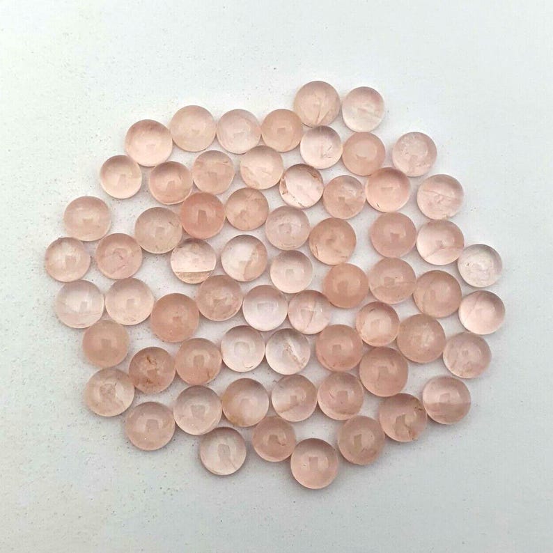 May include: A collection of approximately 50 round, translucent pink rose quartz cabochons. The cabochons are smooth and polished, with a slight shimmer.