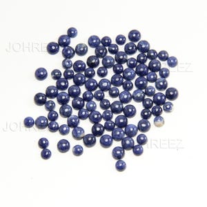 May include: A large group of round, blue gemstone cabochons. The cabochons are smooth and polished, with a slight variation in color.