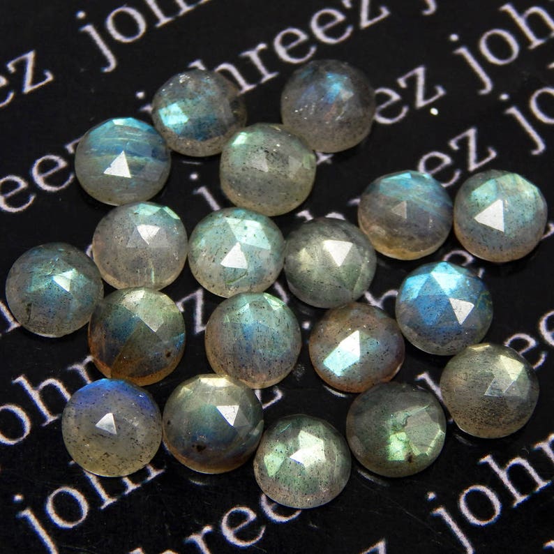 May include: A collection of 16 faceted labradorite gemstones, each with a unique iridescent sheen. The stones are a mix of light and dark grey with blue and green flashes.