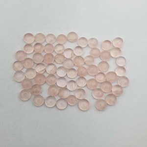 May include: A collection of approximately 50 small, round, translucent pink gemstone beads. The beads are smooth and have a slightly cloudy appearance.