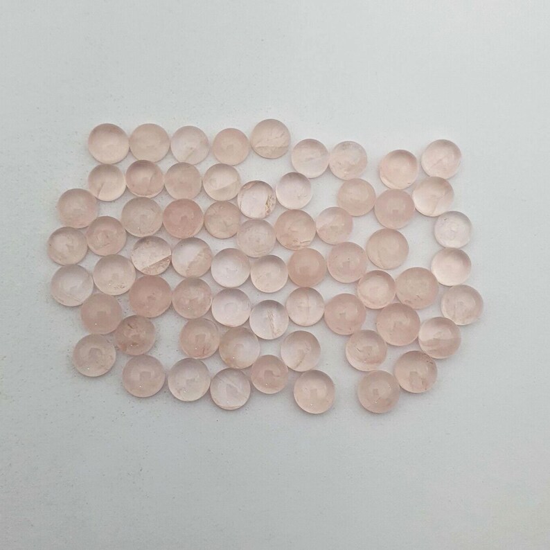 May include: A collection of approximately 50 small, round, translucent pink gemstone beads. The beads are smooth and have a slightly cloudy appearance.