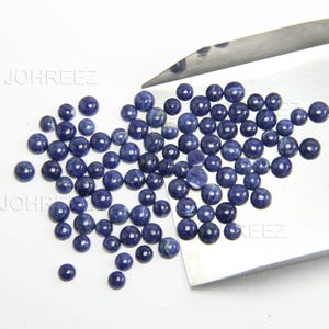 May include: A pile of round, blue gemstone cabochons. The cabochons are smooth and polished, with a slightly iridescent finish.