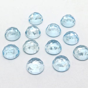 May include: Twelve light blue round faceted gemstones, each with a smooth, polished surface.