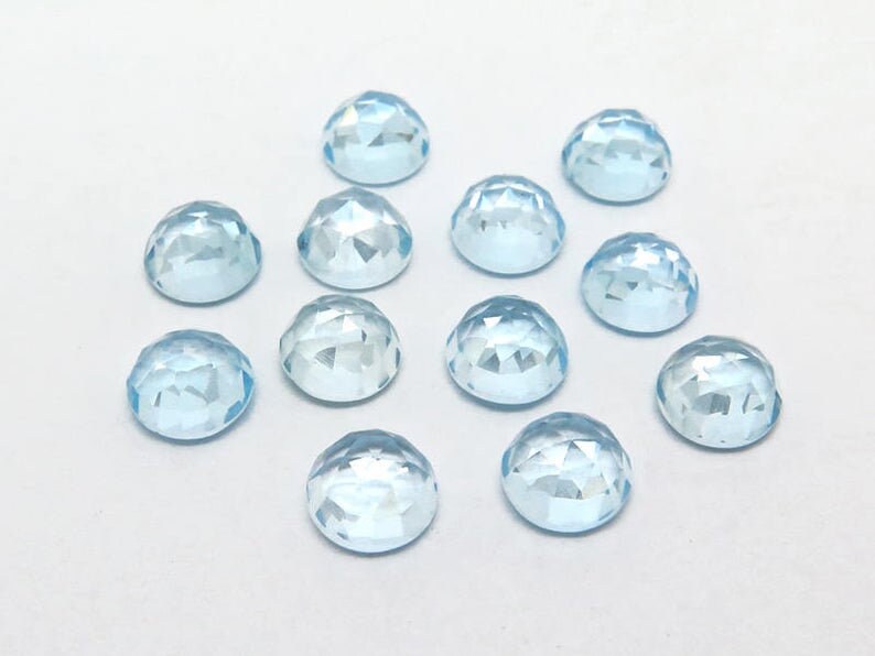 May include: Twelve light blue round faceted gemstones, each with a smooth, polished surface.