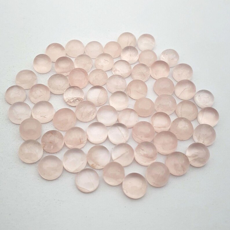 May include: A collection of round, pale pink rose quartz cabochons. The cabochons are smooth and polished, with a translucent appearance.