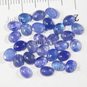 Op de afbeelding: Een verzameling van 25 ovale, blauwe edelstenen. De edelstenen zijn glad en gepolijst, met een lichtblauwe kleur.