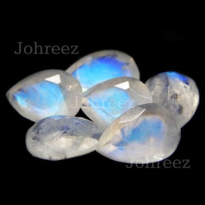 May include: Five pear-shaped moonstone gemstones with iridescent blue and white colors. The stones are faceted and have a smooth, polished finish.