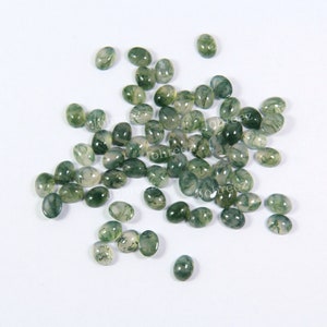May include: A collection of green moss agate cabochons, oval shaped, with a translucent, light green color and white, gray, and green patterns.