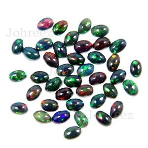 May include: A collection of oval-shaped black opals with green, red, and blue iridescent flashes. The opals are scattered on a white background.