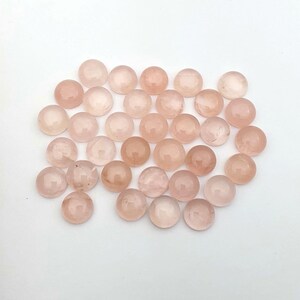 May include: A collection of 30 round, pale pink rose quartz cabochons. The cabochons are smooth and polished, with a slightly translucent appearance.