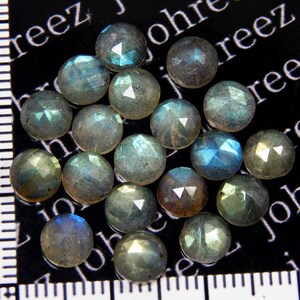 May include: A collection of 18 iridescent, faceted, round labradorite gemstones. The stones are a mix of gray, blue, and green hues with a shimmery, reflective surface.