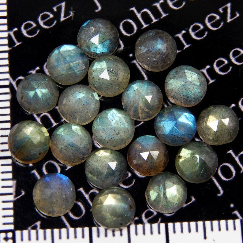 May include: A collection of 18 iridescent, faceted, round labradorite gemstones. The stones are a mix of gray, blue, and green hues with a shimmery, reflective surface.