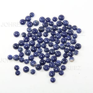 May include: A collection of round, blue gemstone cabochons. The cabochons are smooth and polished, with a variety of shades of blue.