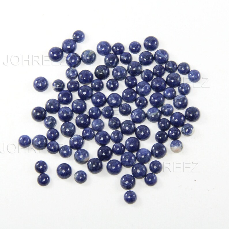 May include: A collection of round, blue gemstone cabochons. The cabochons are smooth and polished, with a variety of shades of blue.