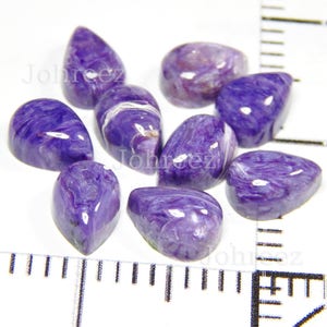 May include: A collection of eight teardrop-shaped purple and white chalcedony gemstones. The stones are polished and have a smooth, glossy finish.