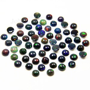 May include: A collection of 40 black opal cabochons, each with a unique iridescent display of colors, including green, red, and blue. The cabochons are round and have a smooth, polished finish.