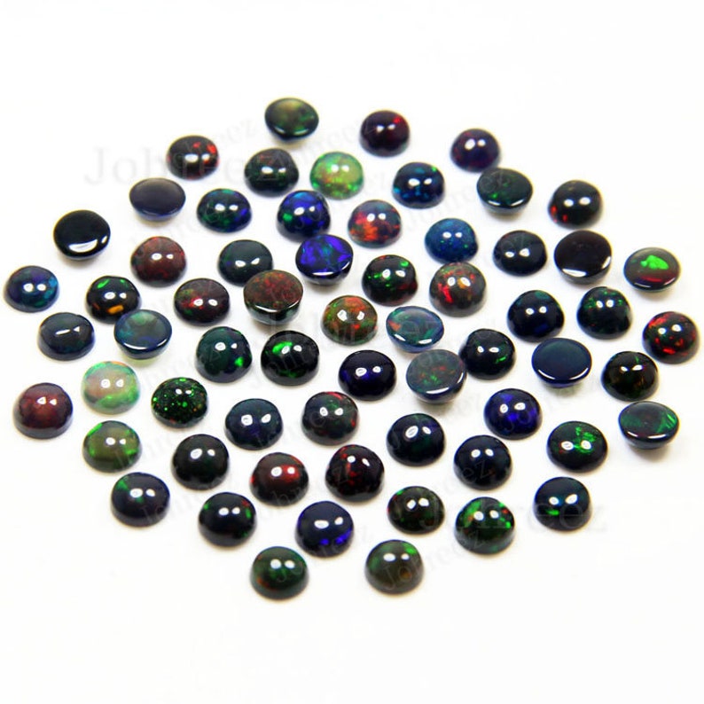 May include: A collection of 40 black opal cabochons, each with a unique iridescent display of colors, including green, red, and blue. The cabochons are round and have a smooth, polished finish.