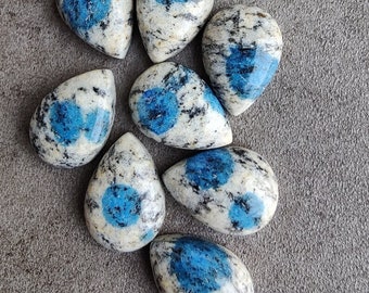 May include: A collection of eight teardrop-shaped blue and white kyanite cabochons. The cabochons are polished and have a smooth, glossy finish.