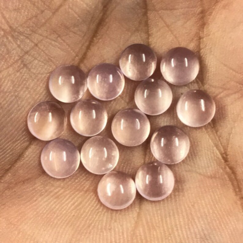 May include: A collection of 14 round, pale pink gemstone cabochons. The cabochons are smooth and polished, with a translucent appearance.