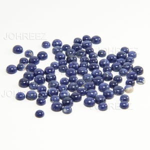 May include: A large group of round, blue-grey gemstone cabochons. The cabochons are smooth and polished, with a slight variation in color and pattern.