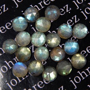 May include: A collection of 18 faceted labradorite gemstones, each with a unique iridescent sheen. The stones are a mix of light and dark gray with hints of blue and green.