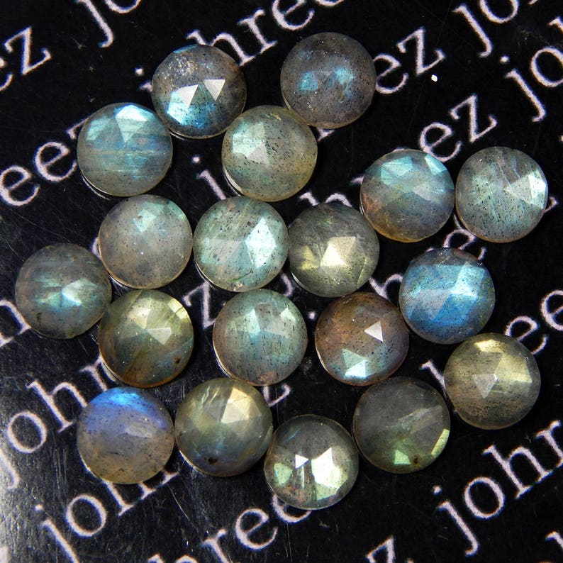 May include: A collection of 18 faceted labradorite gemstones, each with a unique iridescent sheen. The stones are a mix of light and dark gray with hints of blue and green.