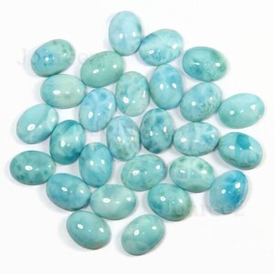 May include: A collection of oval-shaped, light blue gemstone cabochons. The stones have a cloudy, marbled appearance.