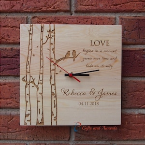 May include: A wooden clock with a quote about love, a bird design, and the names Rebecca & James with the date 04.11.2018. The clock is on a brick wall.