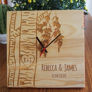 May include: A wooden clock featuring a birch tree design. The clock face has black hands and a red second hand. The clock is personalised with the names "Rebecca & James" and the date "11.04.2020".