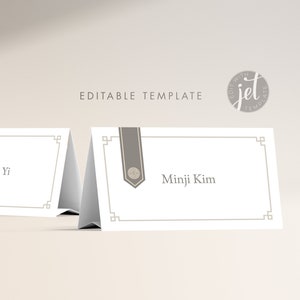 Peut inclure: Deux cartes de place blanches avec des bordures grises et un ruban gris avec un petit motif de cercle gris. Le texte sur les cartes indique "Jacob Yi" et "Minji Kim".