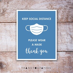 May include: Blue sign with white text that reads "Keep Social Distance" and a white face mask icon. Below the mask is the text "Please Wear A Mask" and "thank you".