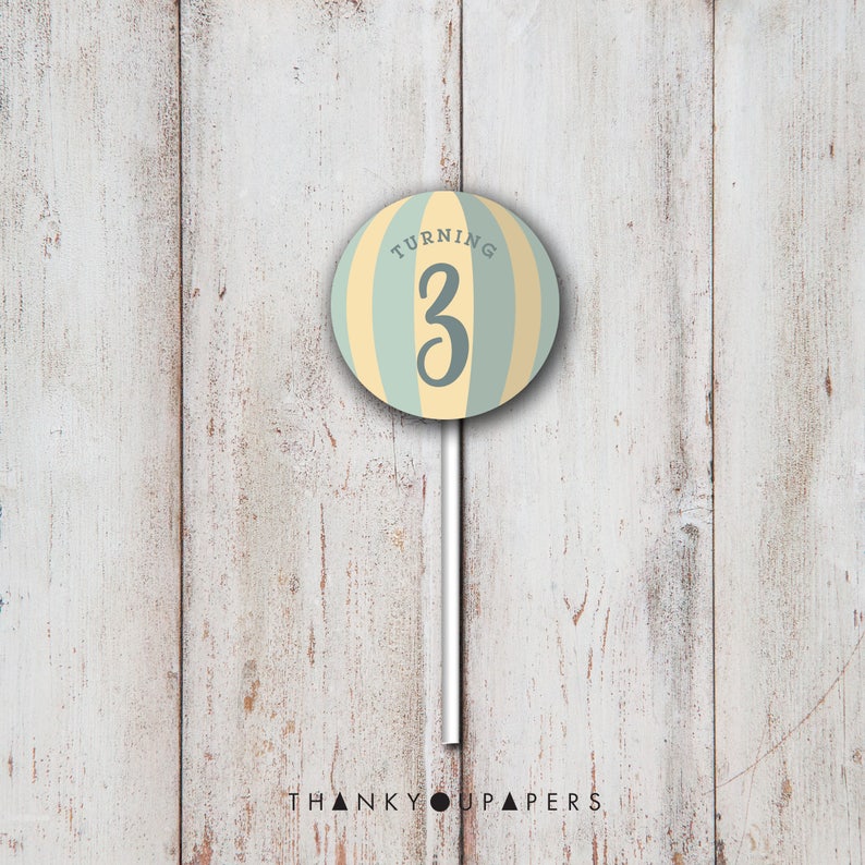 May include: A light blue and yellow striped circle with the text "Turning 3" in gray. The circle is on a white stick.