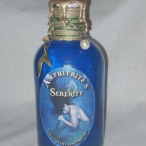 Peut inclure: Une bouteille d'apothicaire en verre bleu avec un sceau de cire doré et une chaîne décorative avec un charme en forme de queue de sirène. L'étiquette indique "Amphitrite's Serenity" avec une illustration de sirène. "The Literary Apothecary" est imprimé en bas.