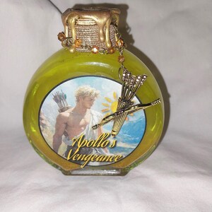 May include: A yellow glass bottle with a gold lid and a gold charm of a bow and arrow. The bottle has a label that says "Apollo's Vengeance".