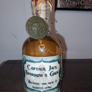May include: A glass bottle with a gold and brown wax seal, a skull and crossbones charm, and a label that reads "Captain Jack Sparrow's Grog Because the rum is always gone."