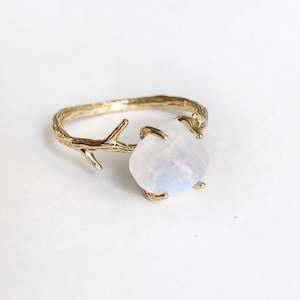 May include: A gold ring with a delicate branch design and a white moonstone gemstone.