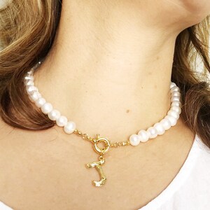 Puede incluir: Un collar de cadena de oro con una hebra de perlas y un dije de oro en forma de la letra 'J'.