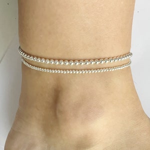 May include: A silver ankle bracelet with two rows of small beads.