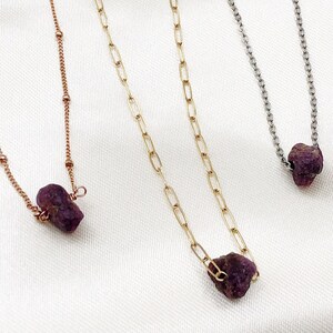 May include: Three delicate necklaces with different chain styles, each featuring a raw, purple gemstone pendant.